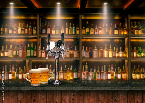 Bar counter with beer tap and full glasses of cold light beer, various alcoholic beverages in the background.