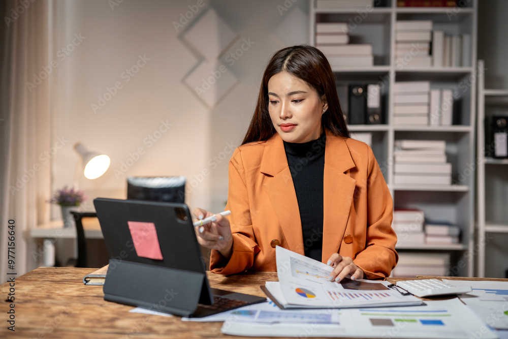 Businesswoman analyzing financial data on digital tablet and charts in office Businesswoman analyzing financial data on digital tablet and charts in office