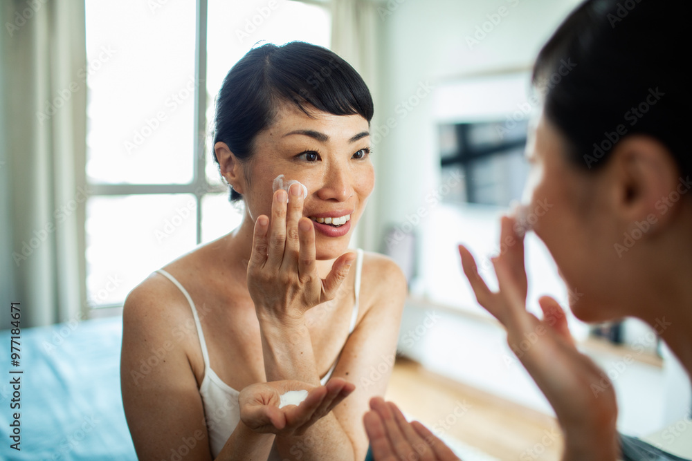 Asian woman applying facial cream in front of mirror Asian woman applying facial cream in front of mirror