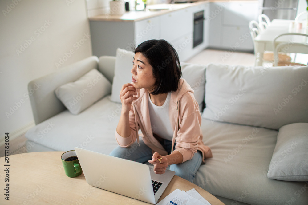 Thoughtful woman working from home with laptop and coffee cup Thoughtful woman working from home with laptop and coffee cup