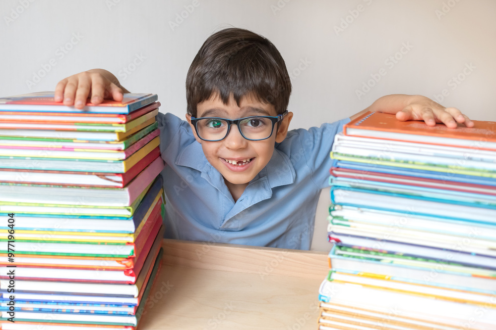 Happy cute boy in glasses with many books enjoys learning isolated on white background. Amblyopia, strabismus. Learning concept Happy cute boy in glasses with many books enjoys learning isolated on white background. Amblyopia, strabismus. Learning concept