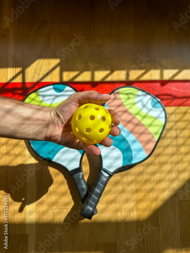  Pickleball paddle with yellow Pickleball with shadow of Pickleball net. 