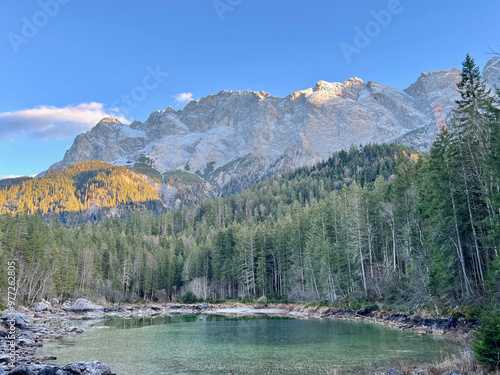 Frillensee, a small lake near Eibsee at the base of Zugspitze, features rocky shores and tall pine forests, set against a backdrop of snow-capped mountains—a stunning alpine scene. photo