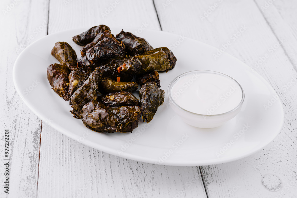 Serving plate presenting stuffed grape leaves dolma with yogurt dip on rustic white table Serving plate presenting stuffed grape leaves dolma with yogurt dip on rustic white table