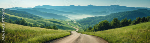 Winding road through lush green hills under a clear blue sky with distant mountains, creating a serene and picturesque landscape.