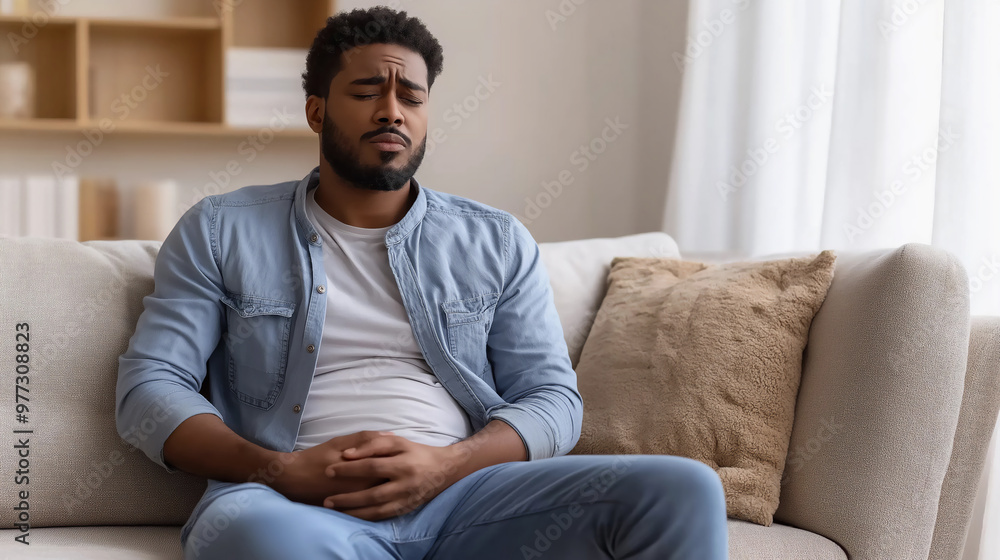 A man with stomach pain is sitting on the sofa at home. A man with stomach pain is sitting on the sofa at home.