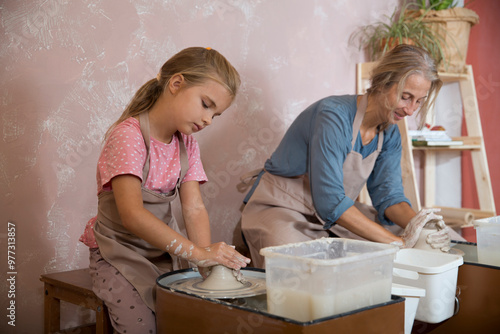 mother and child daughter moulding together from clay on pottery wheel  a pottery class.
