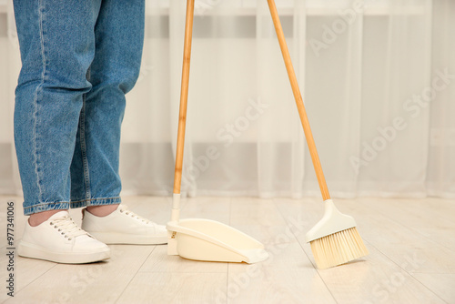 Woman with broom and dustpan cleaning floor indoors, closeup