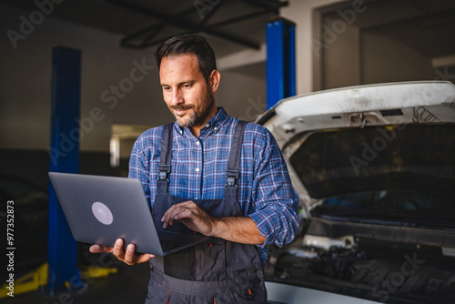 Adult man car mechanic work on laptop in garage with car in background photo