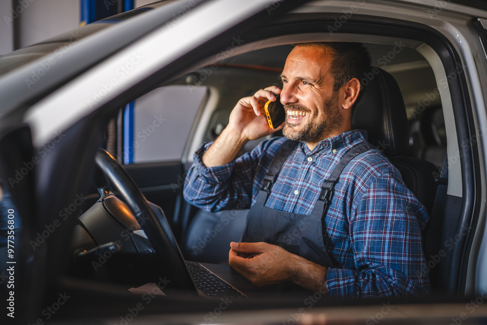 Car mechanic talk on mobile phone while sit in car during repair Car mechanic talk on mobile phone while sit in car during repair