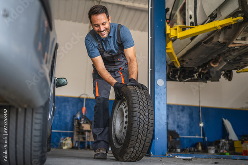 Happy adult man car mechanic work and pushes car tire in auto garage