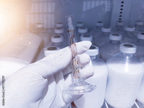 A doctor is holding a Borosilicate glass measuring  to measure doses for laboratory purposes. with background the storage vaccine bottles in showcase. photo