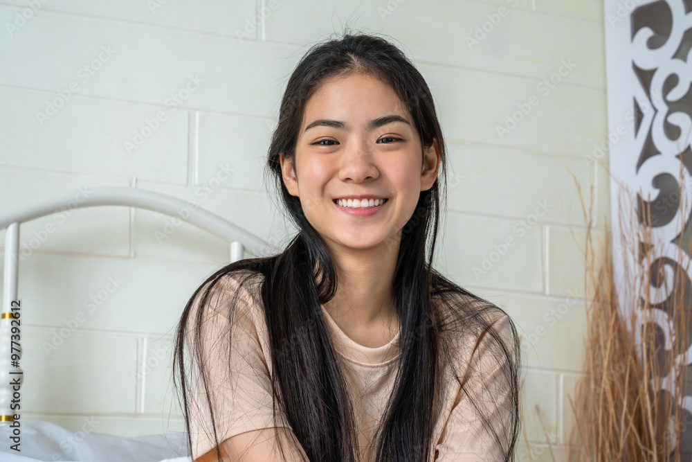 Smiling young Asian woman sitting indoors with natural light, looking at camera Smiling young Asian woman sitting indoors with natural light, looking at camera