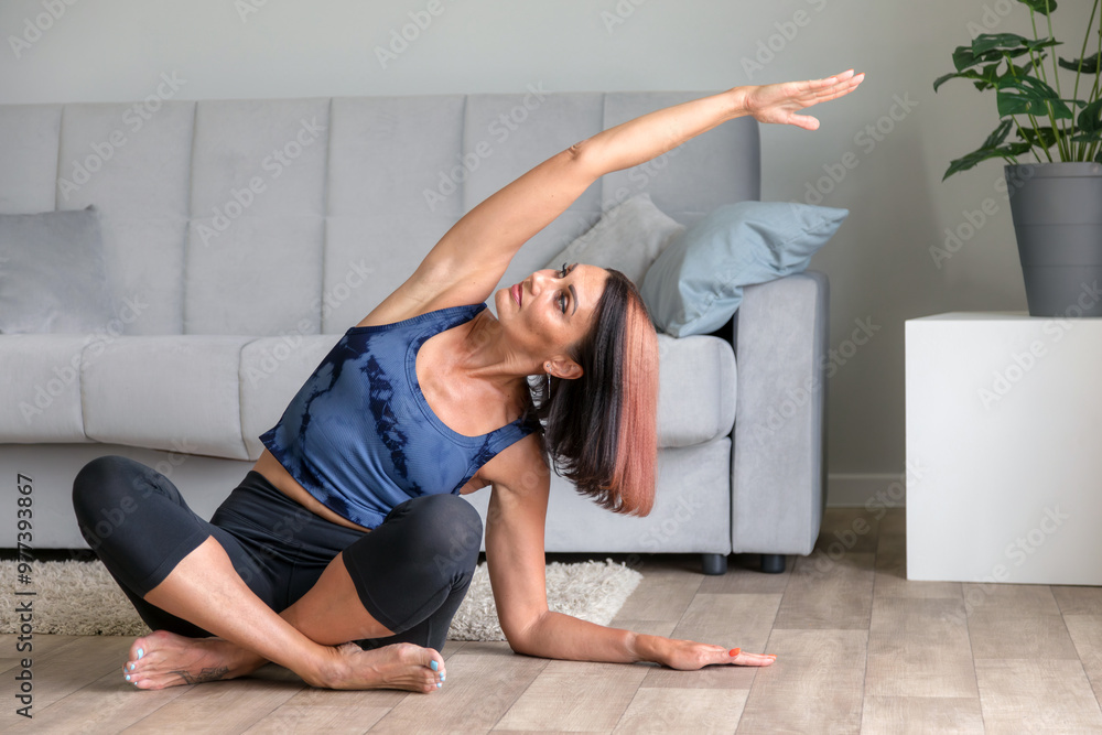 Fototapeta premium Front view of a fit middle age woman doing yoga exercise at home in the living room