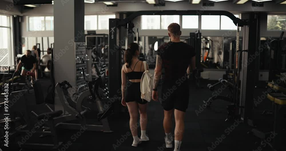 Rear view of a confident girl athlete together with her boyfriend in sportswear walking through the gym before starting a workout Rear view of a confident girl athlete together with her boyfriend in sportswear walking through the gym before starting a workout