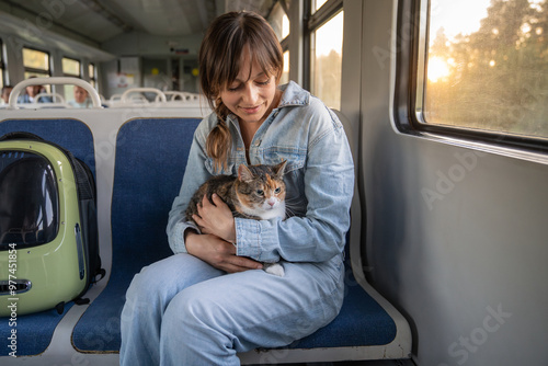 Excited cute cat traveling in electric train on woman owner lap next to window. Satisfied female uses public transportation with kitty hugging while taking out of carrier. Pet lover in trip. photo