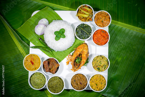 Traditional Bengali dishes such as bhorta, bhaji, fish curry, and vegetable curry are served in white ceramic pots and with Banana leaves. photo