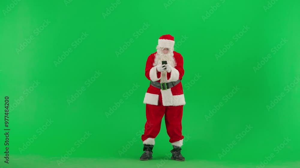 Portrait of man dressed as Santa on chroma key green screen background. Santa Claus in red outfit holding smartphone reading news amazed face. Portrait of man dressed as Santa on chroma key green screen background. Santa Claus in red outfit holding smartphone reading news amazed face.