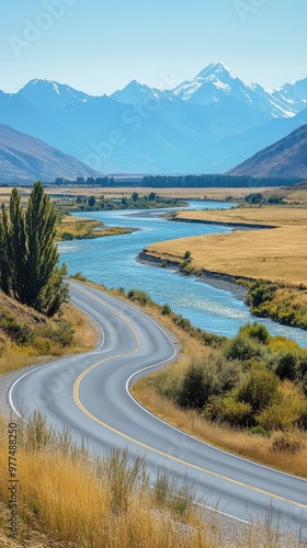 Serene landscape featuring a winding road along a river, surrounded by mountains and golden grass, perfect for adventure and travel themes.