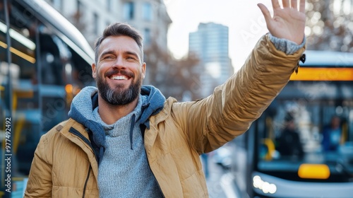 A bearded man in a yellow jacket waves exuberantly while waiting for the bus in an urban location, surrounded by city scenery, exuding confidence and joy. photo