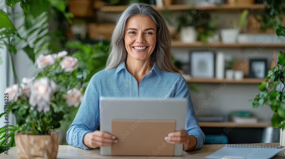 A woman with gray hair uses a tablet while seated in a modern office surrounded by green plants, symbolizing experience and technology blending seamlessly. A woman with gray hair uses a tablet while seated in a modern office surrounded by green plants, symbolizing experience and technology blending seamlessly.