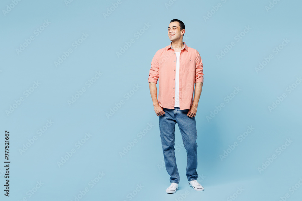 Full body smiling happy young middle eastern man he wear pink shirt white t-shirt look aside on empty blank area isolated on plain pastel light blue cyan background studio portrait. Lifestyle concept. Full body smiling happy young middle eastern man he wear pink shirt white t-shirt look aside on empty blank area isolated on plain pastel light blue cyan background studio portrait. Lifestyle concept.