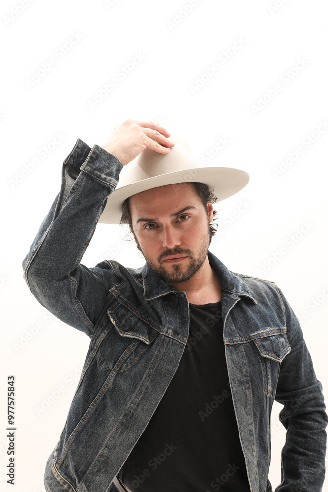 Bearded man wearing denim jacket and fedora hat over white wall. Bearded man wearing denim jacket and fedora hat over white wall.