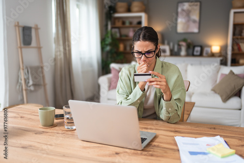 Confused young woman having problem with blocked credit card making rejected unsecure online payment using laptop at home, invalid expired account, transaction failed, money withdraw impossible, debt photo