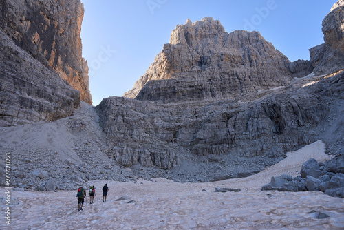 Hikers crossing a snow massive on a way to via ferrata in Brenta Dolomites. Mountain illuminated by the first rays of the sun. Vacation in Italy. Active lifestyle.  