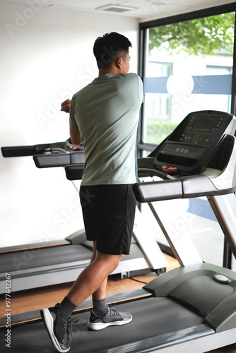 Young asian man stretching hands in fitness club. Cardio workout, guy warming up, preparing for running on treadmill. Healthy lifestyle, guy training in gym.