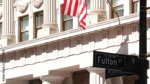 New York City crossroad, Fulton street intersection road sign. Manhattan downtown financial district architecture, NYC, United States. American flag and roadsign near Broadway.
