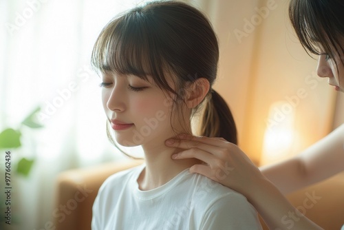 Japanese woman in casual clothes is receiving a neck massage from a physical therapist for chronic stiff neck, with the physical therapist's hands lightly holding her shoulders.