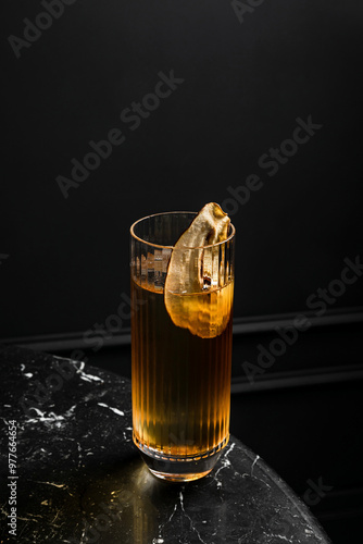 An alcoholic cocktail in a highball glass garnished with dried pear slice served on ice in a bar