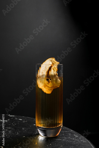 An alcoholic cocktail in a highball glass garnished with dried pear slice served on ice in a bar