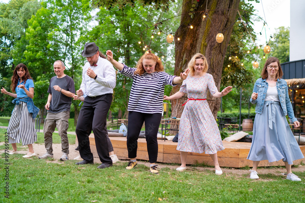 Fototapeta premium Cheerful dance party outdoors, featuring individuals of different ages enjoying the festive ambiance under illuminated string lights. They are dancing swing dance in summer city park