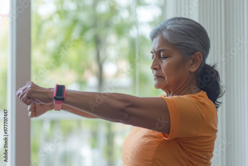 Elderly woman is wearing a smartwatch and stretching her arms while exercising indoors Free Download Elderly woman is wearing a smartwatch and stretching her arms while exercising indoors - GFXLoad