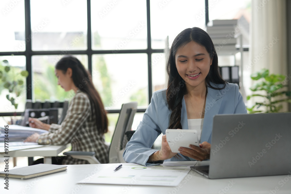 Confident and positive asian businesswoman performing financial calculations in a modern office, illuminated by bright natural light Confident and positive asian businesswoman performing financial calculations in a modern office, illuminated by bright natural light
