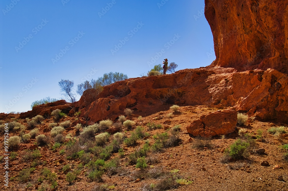 Woman standing at the foot of towering red laterite cliffs in the ...