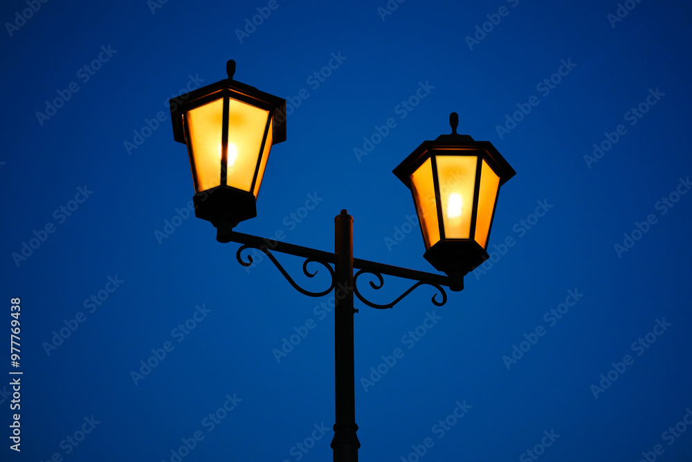Retro style street lantern with bright yellow light against the evening deep blue sky. Vintage outdoors lamp. Retro style street lantern with bright yellow light against the evening deep blue sky. Vintage outdoors lamp.