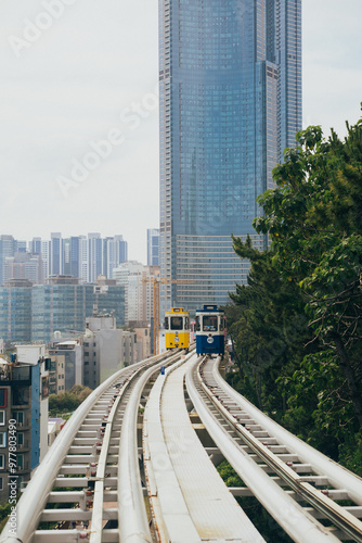 Modern monorail trains travel on elevated tracks near urban buildings in Haeunde Blueline Park during daylight photo