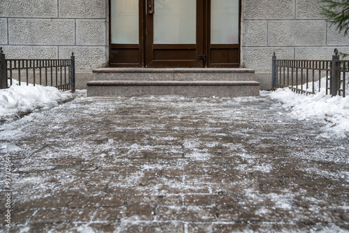 Icy sidewalk. Ice crust in front of building entrance, sidewalk tile covered with ice, slippery street. Winter weather.