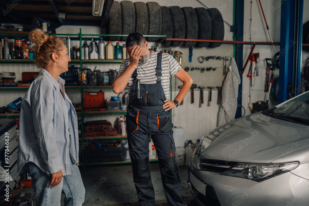 Fototapeta premium Mechanic is doing facepalm at workshop while woman is smiling at him.