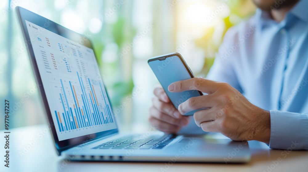 A professional managing finances on both a smartphone and laptop, reviewing spending categories and data charts. The focus is on the seamless integration of mobile and desktop tool A professional managing finances on both a smartphone and laptop, reviewing spending categories and data charts. The focus is on the seamless integration of mobile and desktop tool