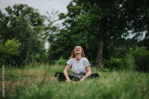 A joyful woman in white top meditating outdoors, enjoying tranquility in a lush green forest setting under the open sky.