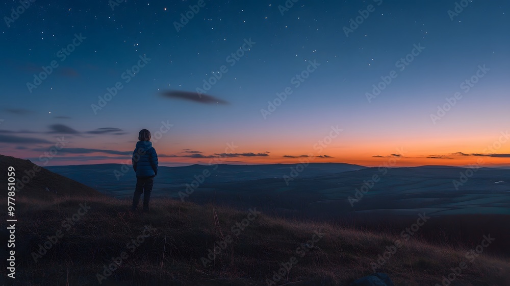 Obraz premium A child standing on a hilltop at dusk watching as the first stars appear in the deepening sky.