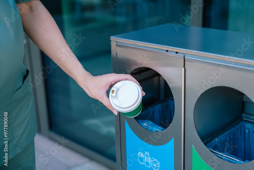 Close up of a female hand throwing empty paper cup to the waste bin photo