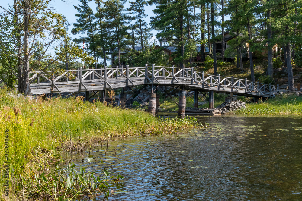 An Old Cedar Footbridge Over a Body of Water Surrounded by Pine Trees and Rustic Cottages An Old Cedar Footbridge Over a Body of Water Surrounded by Pine Trees and Rustic Cottages