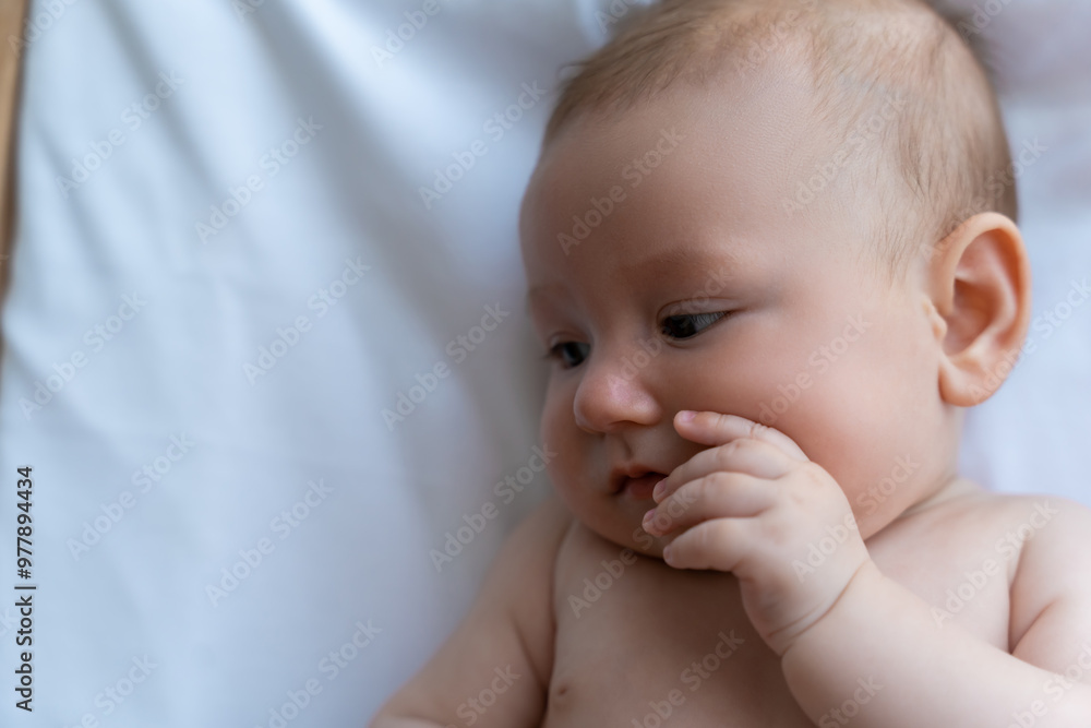 Sweet little baby lying on white sheet looking away, copy space Sweet little baby lying on white sheet looking away, copy space