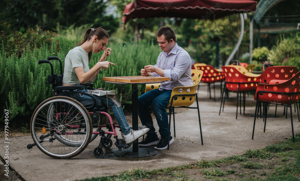 A young boy with Down syndrome and a girl in a wheelchair play backgammon together at an outdoor cafe, highlighting inclusion and friendship. A young boy with Down syndrome and a girl in a wheelchair play backgammon together at an outdoor cafe, highlighting inclusion and friendship.