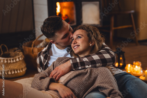 Beautiful young loving couple relaxing near fireplace in bed at home. Happy spouses enjoying lazy romantic winter cozy morning in bedroom. Candles, garlands, countryside interior. Romantic date